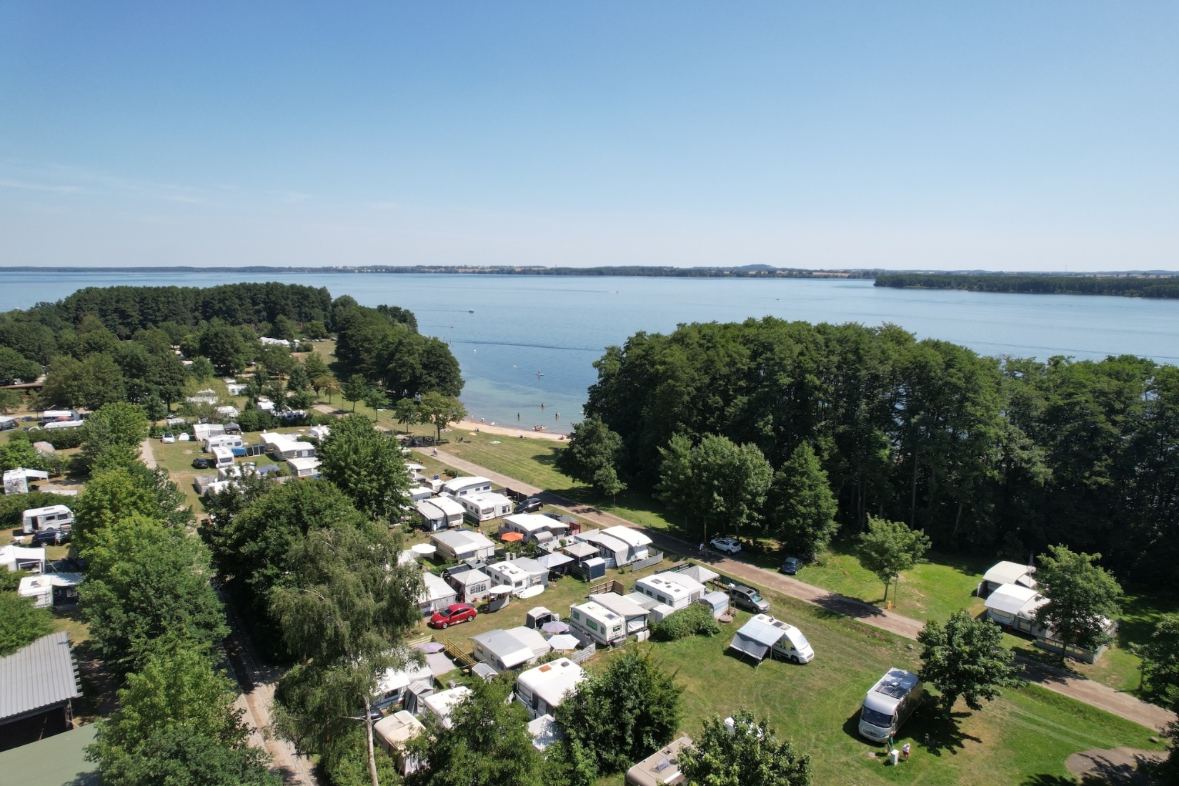 Eine Luftaufnahme des Ferienpark Seehofs, welcher direkt am Schweriner See liegt. Die Aufnahme ist zur Zeit der Hochsaison im Sommer entstanden, in der viele Gäste zur Ruhe und Entspannung bei uns eine Auszeit gesucht haben. BVCD e.V.